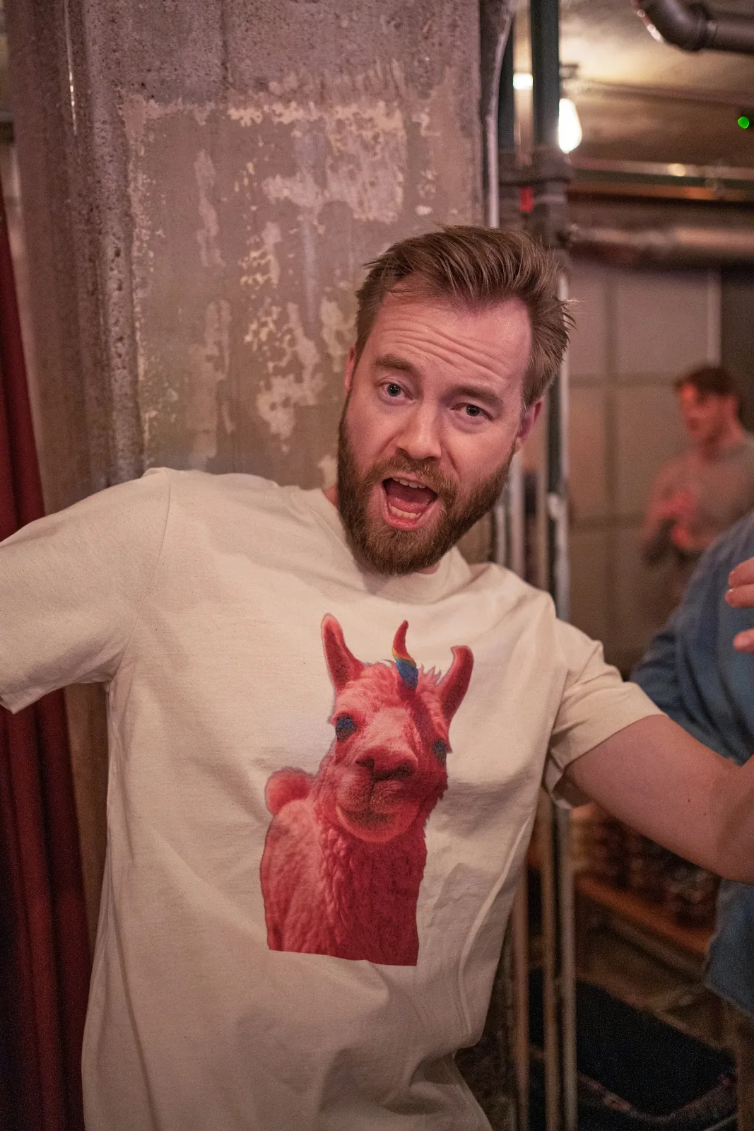 An attendee with arms spread wearing a pink LLaMacorn T-shirt. Helsinki.