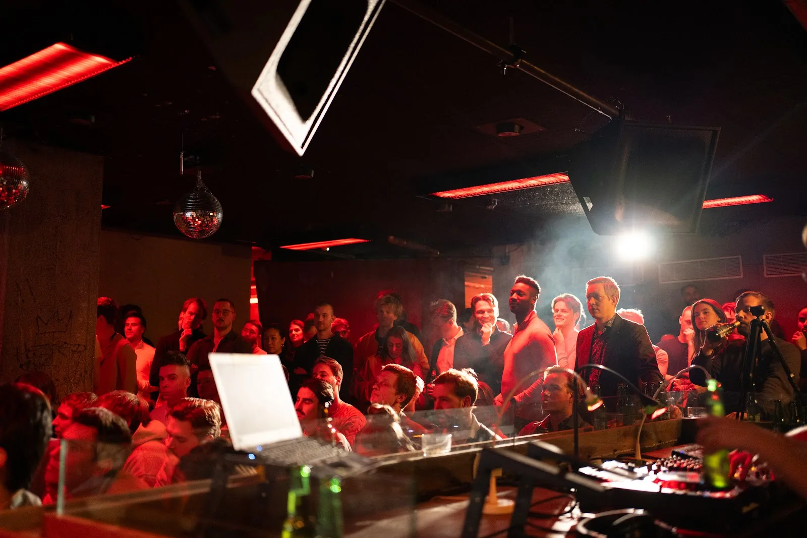 A packed audience beneath disco balls and red lights, seen across the mixing desk. Helsinki.
