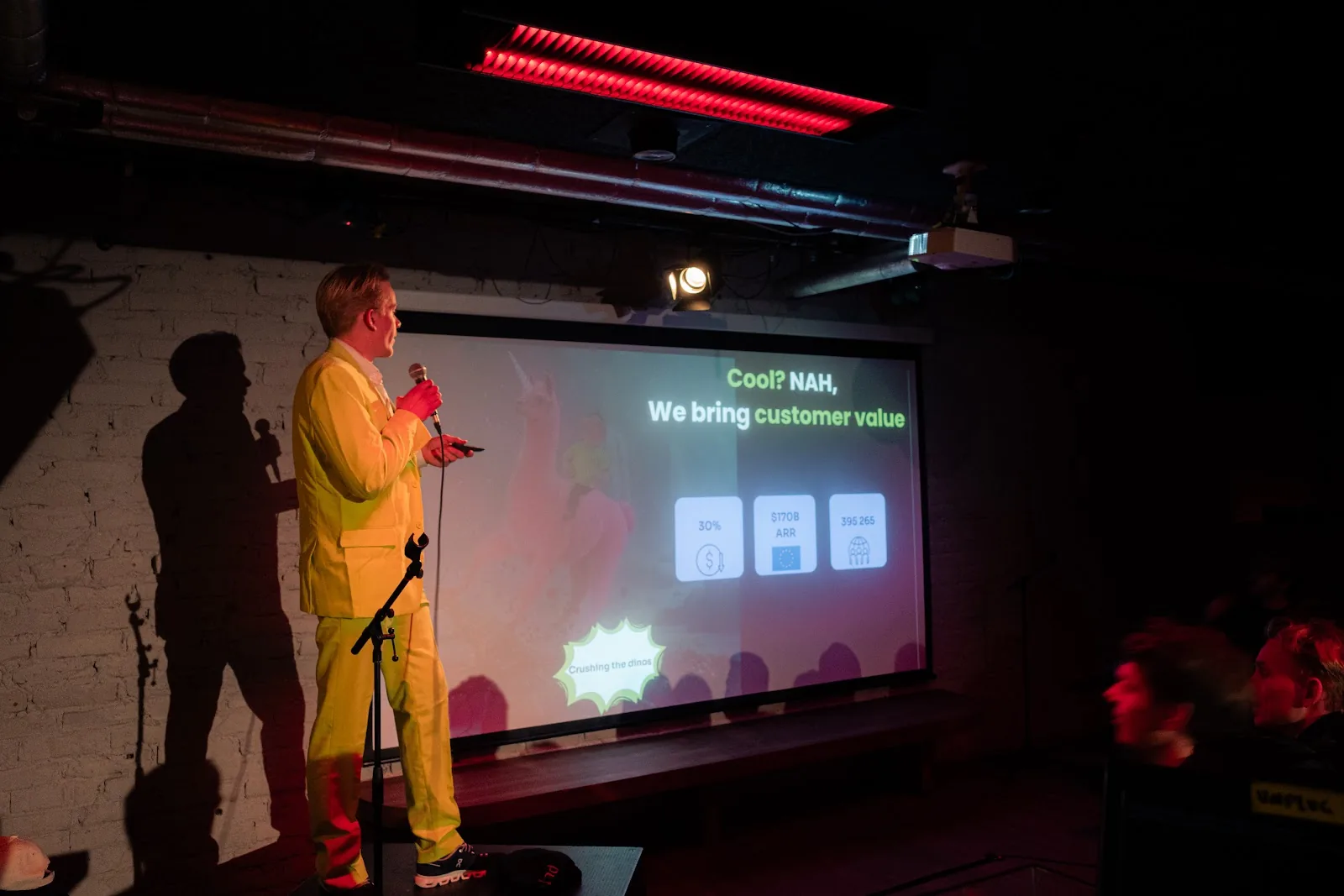 A man in a neon yellow suit holding a microphone on the Helsinki stage.