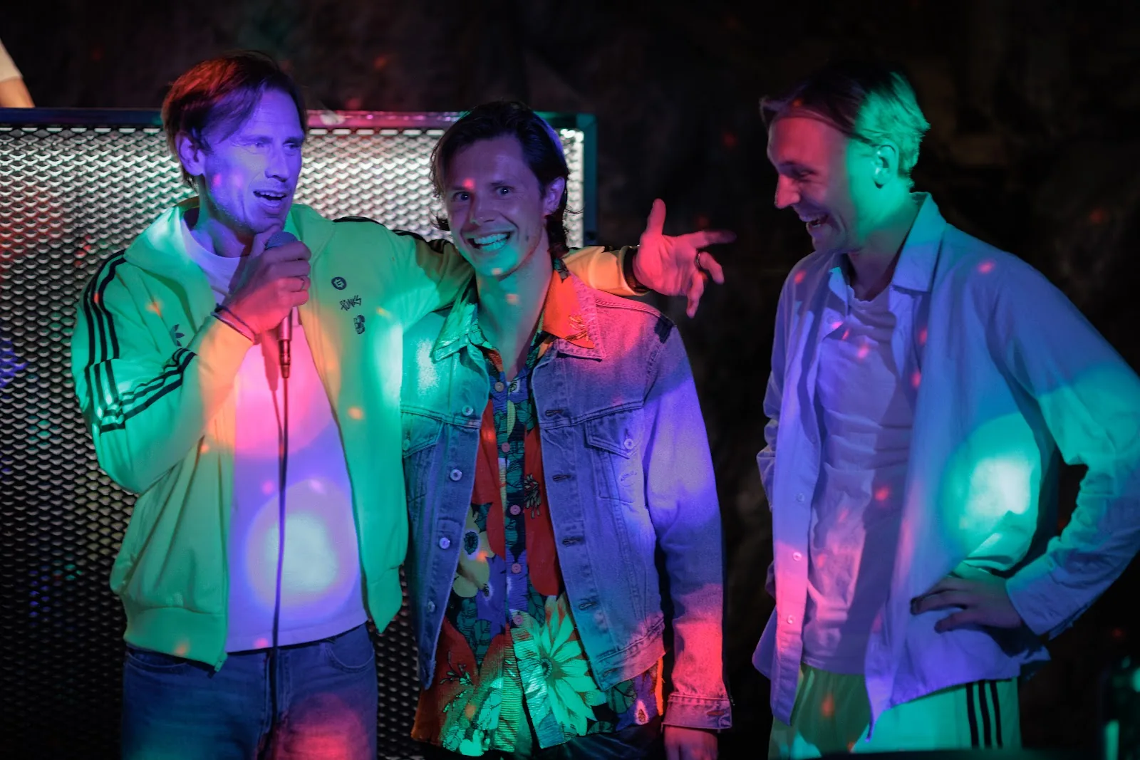 Three people laughing beside the DJ booth under coloured lights, one holding a microphone. Stockholm.
